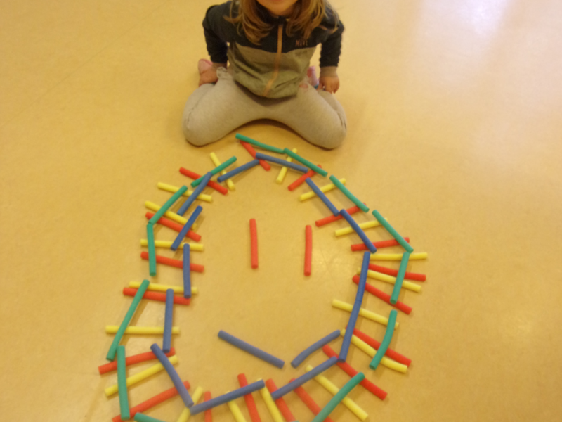 Ein Kind das auf dem Boden sitzt und ein großes  Gesicht aus kleinen Spielzeug-Röllchen vor sich liegen hat.