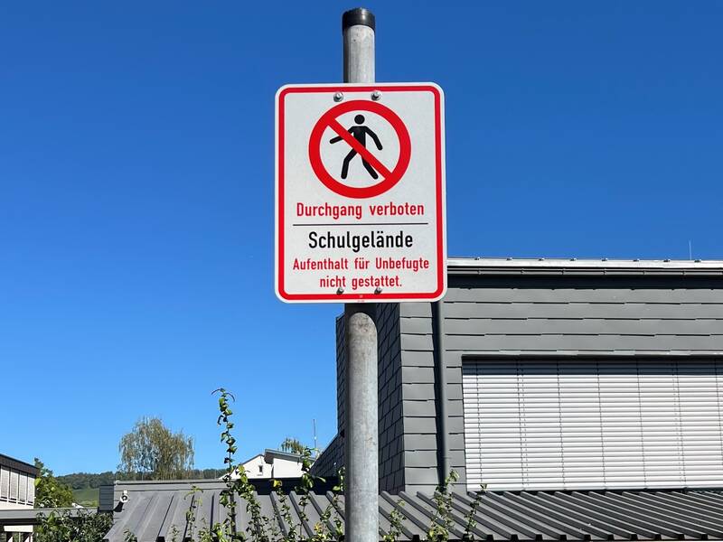 Ein Schild vor einem Gebäude zeigt mit einem durchgestrichenen Fußgänger, dass der Durchgang auf dem Schulgelände für Unbefugte verboten ist.