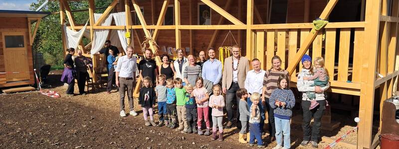 Eine Gruppe von Erwachsenen und Kindern steht vor einem hölzernen Gebäude und posiert für ein Foto.