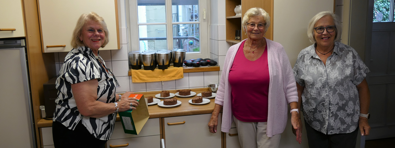 Drei Frauen stehen in einer Küche und haben mehrere Teller mit Kuchenstücken vor sich.