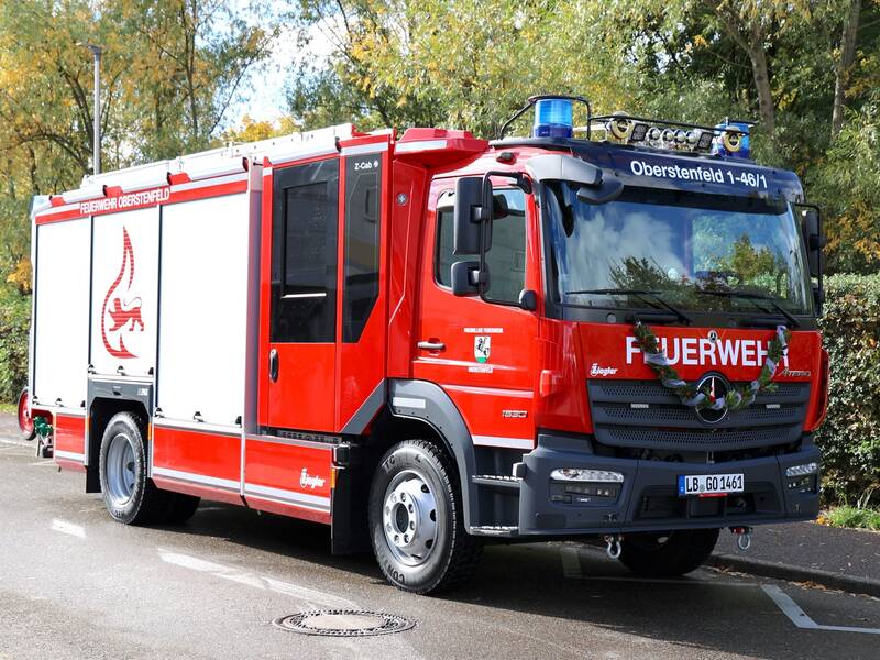 Ein rotes Feuerwehrfahrzeug mit der Aufschrift "FEUERWEHR" steht auf einer Straße, flankiert von Bäumen im Hintergrund.